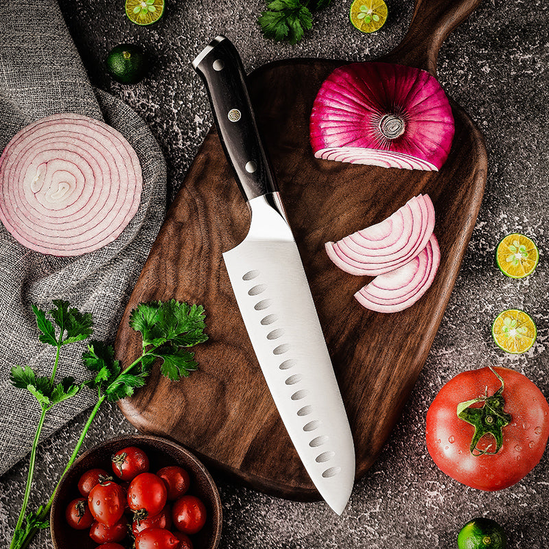 Wooden cutting board with sliced red onion, knife, and fresh vegetables on a dark surface