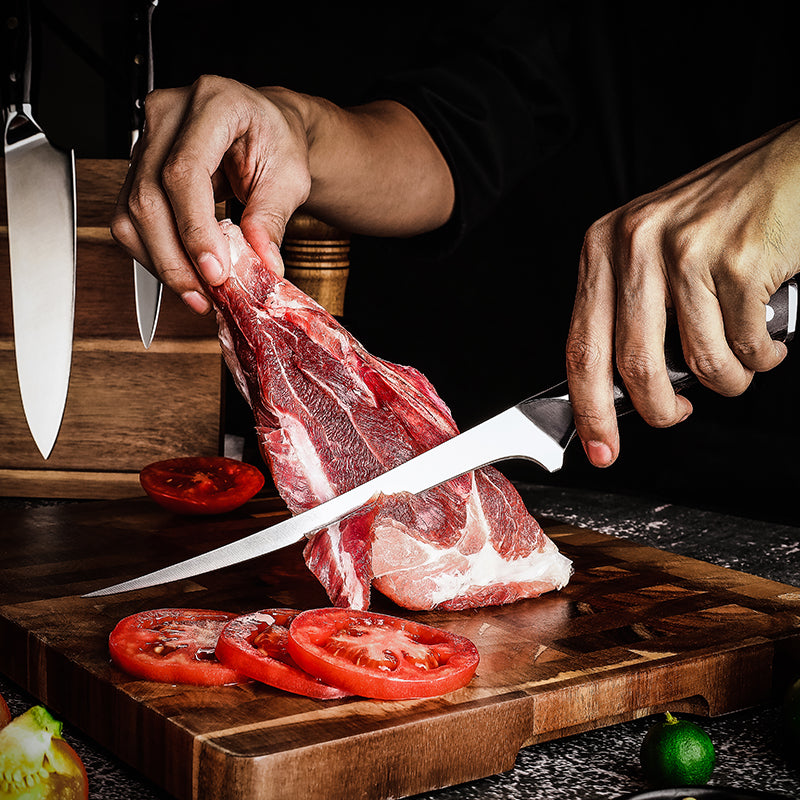Person cutting raw meat on a wooden cutting board with tomatoes and a meat special knife with flexible blade.