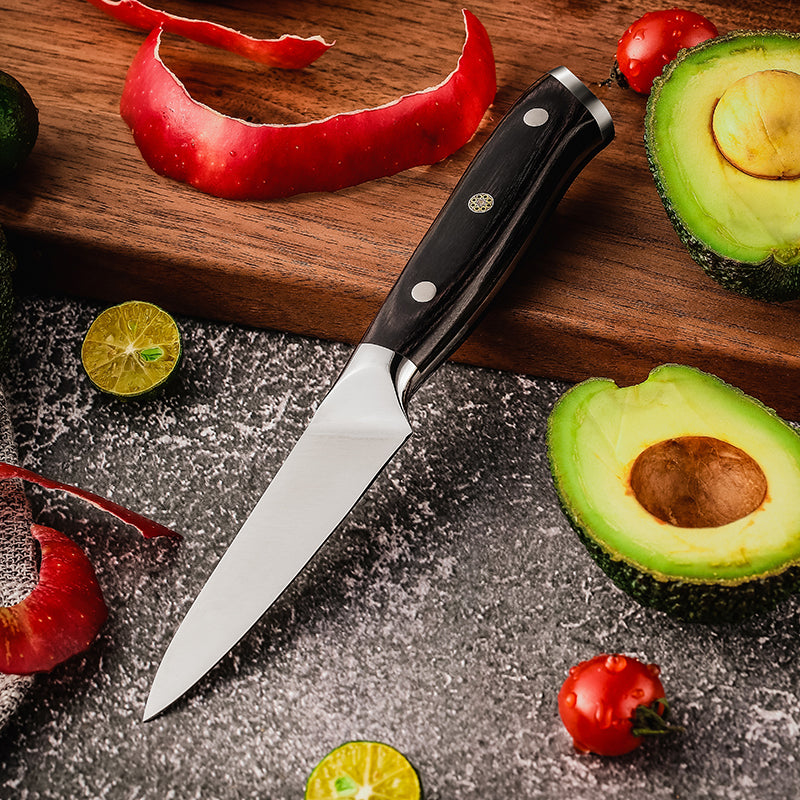 Knife with black handle on a wooden cutting board surrounded by sliced avocados, limes, and red peppers.