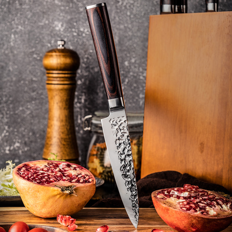 Knife with decorative blade design on a wooden cutting board with pomegranates and a pepper grinder.
